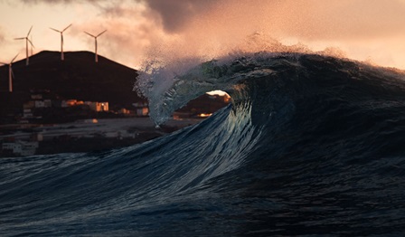 Wave at sea with wind turbines on land in the distance