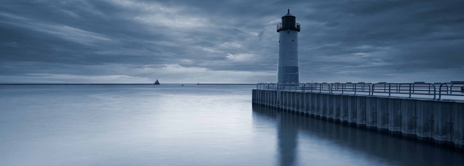 image of a lighthouse next to a pier with ship sailing in the distance