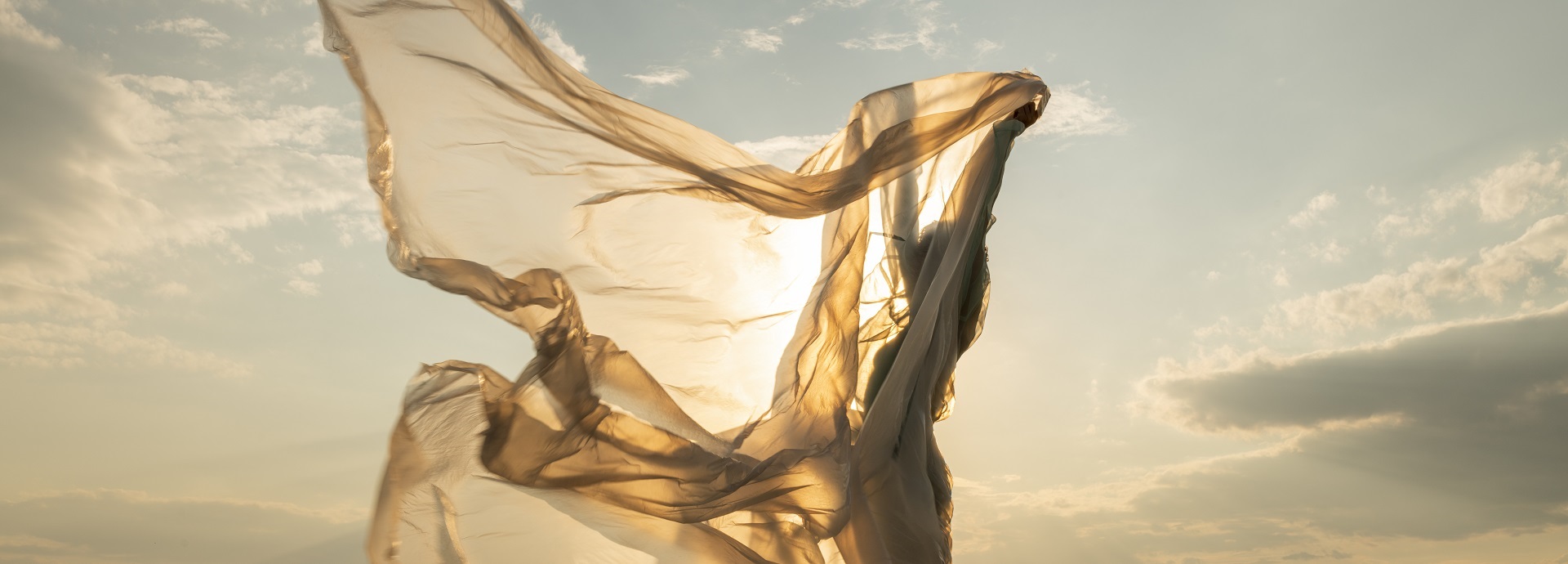 A woman waving a golden transparent fabric in sunshine