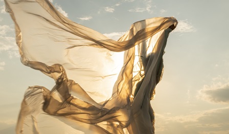 A woman waving a golden transparent fabric in sunshine
